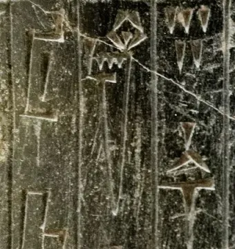 Close-up of the Iddi-Ilum statuette showing deeply carved cuneiform script on a weathered stone surface.