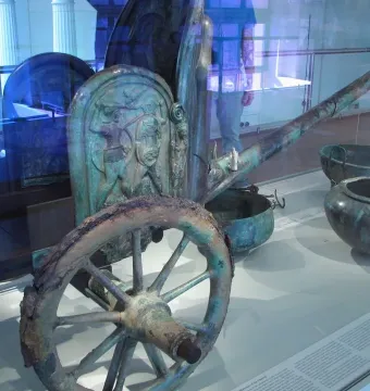 Monteleone Chariot displayed behind glass with a spoked wheel, decorated relief panel, and long shaft visible.