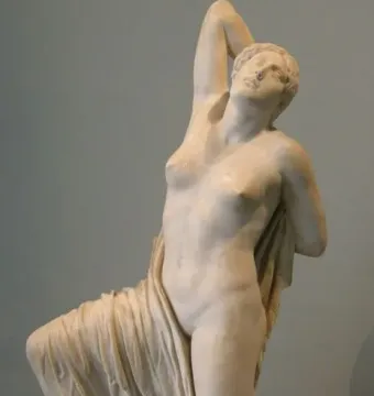 Niobid sculpture in marble, shown kneeling with one arm raised and her head tilted back.