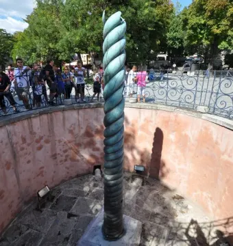 The Serpent Column stands in a sunken pit behind a decorative fence, with visitors gathered around it.