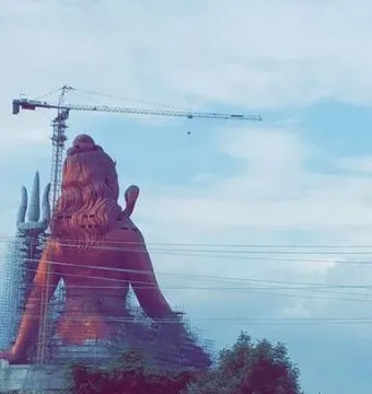 Statue of Belief seen from behind, with scaffolding, a crane, and a cloudy sky
