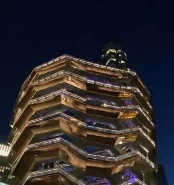 The Vessel lit up at night with golden lights and people gathered below.