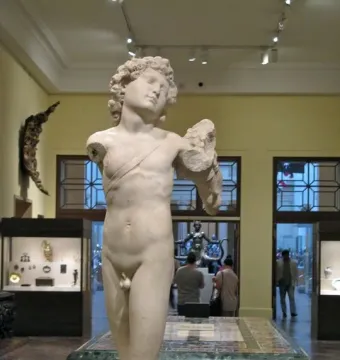 Incomplete marble statue of the Young Archer, showing a nude youthful male figure with curly hair and a diagonal band across the torso.