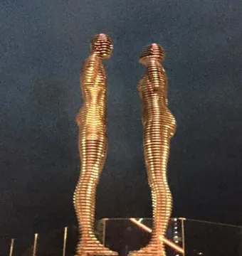 Ali and Nino sculpture with two golden segmented figures facing each other at night