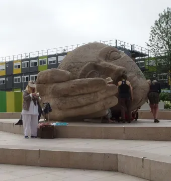 Écoute, a large stone sculpture of a reclining human head with a hand cupped near its ear, in a Paris plaza.