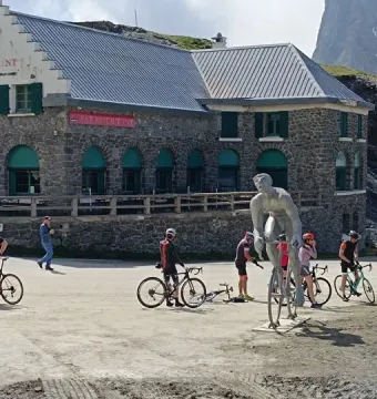 Géant du Tourmalet statue of a cyclist beside a mountain restaurant, with cyclists and bikes in the foreground