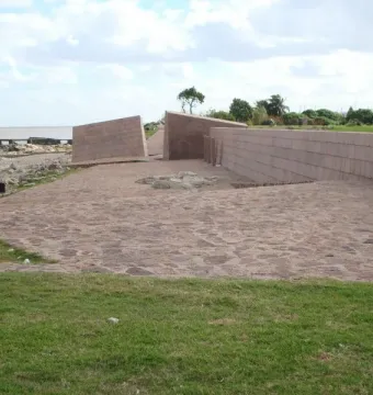 Holocaust Memorial with light pink granite walls beside a rocky shoreline and water.