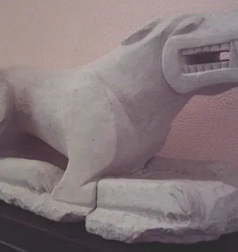 Leona de Baena stone lioness sculpture on a dark base against a pale wall.