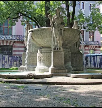 Nornenbrunnen stone fountain with three draped female figures and cascading water in Munich.