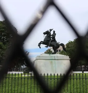 Andrew Jackson statue on a rearing horse, seen through a blurred fence with trees and buildings in the background.