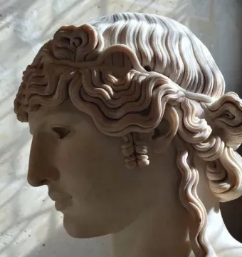 Marble head and upper torso of Antinous Mondragone shown in profile, with elaborately carved wavy hair.