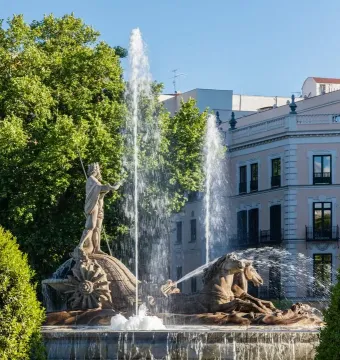 The Fountain of Neptune in Madrid with a crowned figure holding a trident and horses surrounded by tall water jets.