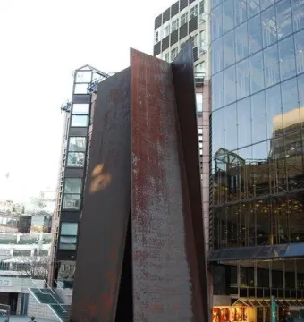 Fulcrum, a large rusty metal sculpture with leaning panels forming a triangular opening in an urban plaza.