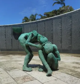Bronze figures at the Holocaust Memorial beside a curved wall covered with inscriptions.
