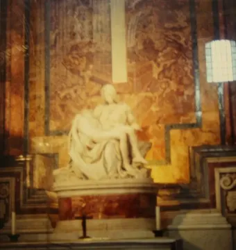 Michelangelo\'s Pietà in white marble, with the draped Virgin Mary holding Christ across her lap inside a patterned church interior.