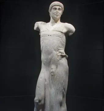 The Motya Charioteer, a white marble male statue missing its arms, shown against a dark background.