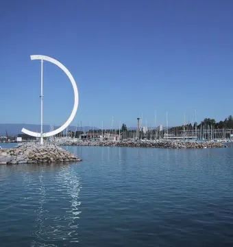 Éole, a large white D-shaped metal sculpture on a rocky breakwater with a marina in the background.