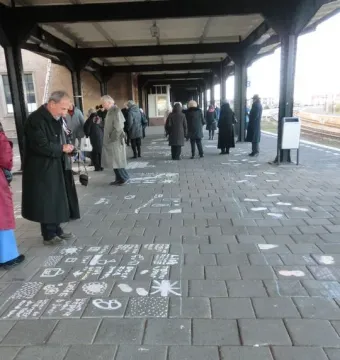 People stand on a covered train platform beside chalk drawings and symbols spread across the paving stones.