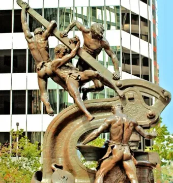Mechanics Monument shows four muscular male figures working together around a large industrial machine.