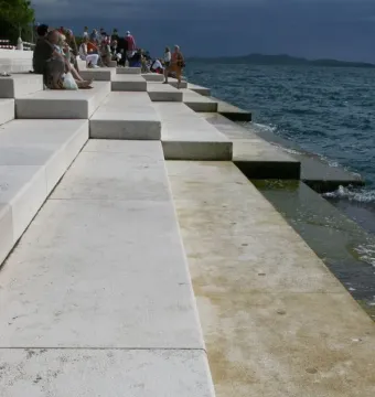 Concrete steps of the Sea Organ descending into a dark, choppy sea, with people seated on the upper levels.