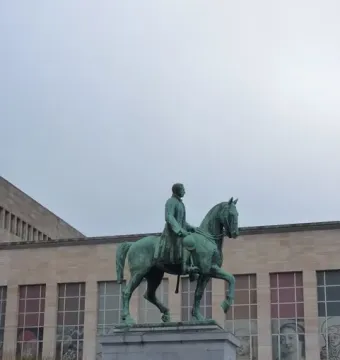 Albert I equestrian statue on a stone plinth with a modern building in the background.