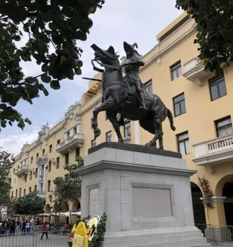 Francisco Pizarro equestrian statue on a stone pedestal, surrounded by floral wreaths and metal barricades in Lima.