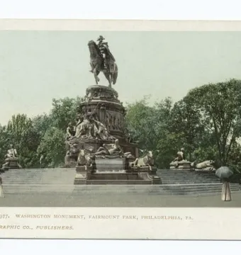 The Washington Monument in Fairmount Park rises above a tiered stone plaza with several people standing nearby, including one holding an umbrella.