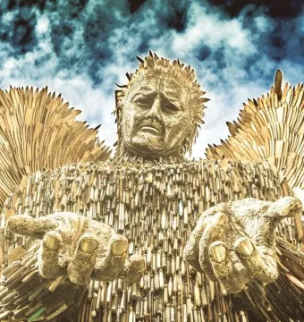 The Knife Angel sculpture shown from below against a cloudy sky, with outstretched hands and wing-like forms made from blades and knife handles.