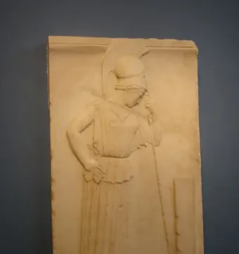 Mourning Athena relief showing a helmeted female figure in profile, leaning on a staff beside a rectangular stele.