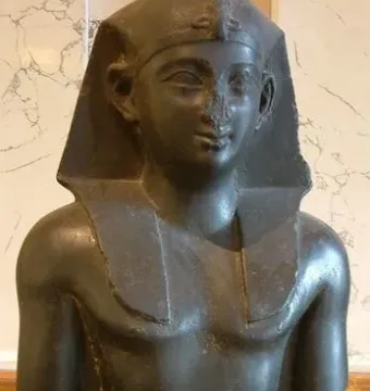 Fragmentary bust of a Ptolemaic king with an Egyptian nemes headcloth, broad collar, and broken nose.