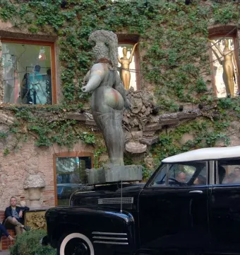 Rainy Taxi sculpture at the Dalí Theatre-Museum, with a black vintage car, a nude bronze figure above it, and ivy-covered stonework behind.