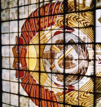 Stained glass window with the Soviet emblem, including a hammer and sickle, wheat sheaves, and a red star.