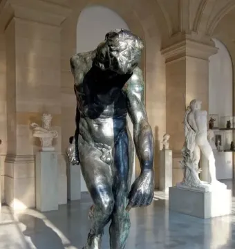 The Shade, a dark bronze male figure standing with bowed head in a museum hall.