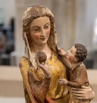 Virgin on a Wide Throne, a painted wooden sculpture of a woman holding a child and a small round fruit.