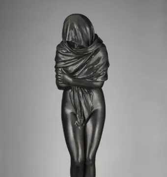 Winter bronze sculpture of a draped figure standing with arms crossed on a circular base.