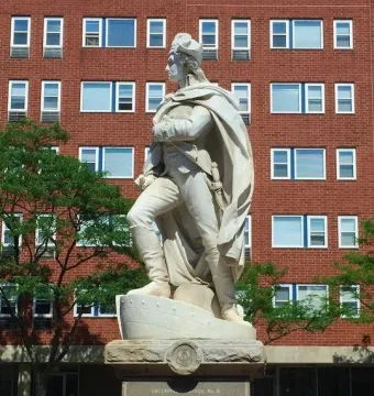 George Washington statue on a tiered pedestal in front of a brick building, with trees on either side.