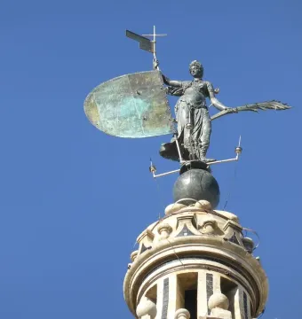 The Giraldillo sculpture of a robed woman holding a shield and palm frond against a blue sky.