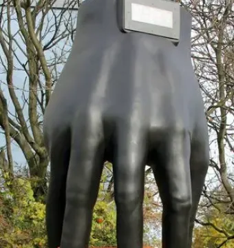 Hand mit Uhr sculpture by Joachim Schmettau, showing a dark metal hand on a tall pedestal with a clock display at the wrist.