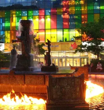 La Joute bronze fountain with abstract figures and flames on the water at night.