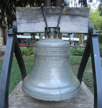 The Liberty Bell displayed outdoors on a wooden beam with metal supports and a visible crack.