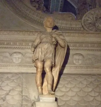 Saint Proculus marble statue of a young man in a short tunic and draped cloak against an ornate carved wall.