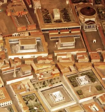 An aerial view of a Roman city scale model with a prominent white column in an open plaza, representing the Antoninus Pius Column area.