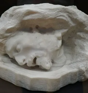 Head of Saint John the Baptist, a textured stone sculpture of a face with closed eyes and an open mouth set in a rough enclosure.