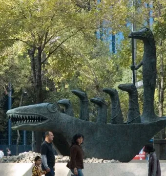 Leonora Carrington’s crocodile sculpture stands among trees with people walking nearby.