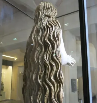Back and right side of the Mary Magdalene statue, with long wavy hair covering the carved figure behind glass.