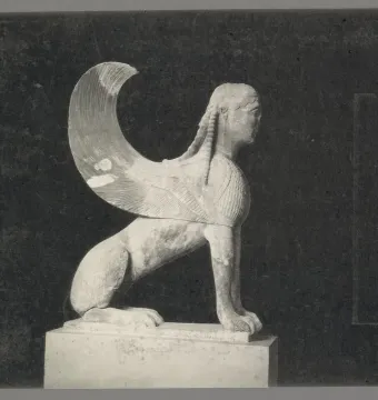 Weathered stone Sphinx of Naxos sculpture in profile with a large wing, shown on a pedestal.