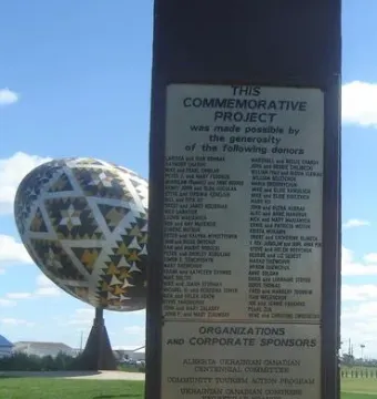 The Vegreville egg sculpture stands in the background with a commemorative plaque in the foreground on grass.