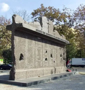Monument to the Victims of the Wola Massacre with a rough-hewn granite face covered in names and dark indentations.