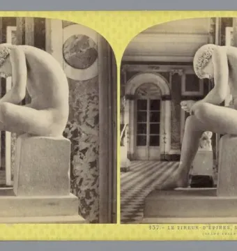 The Boy with Thorn statue, a nude boy seated on a pedestal and bent over his foot in an ornate interior.