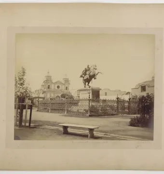 The Equestrian Statue of Simón Bolívar stands on a tall pedestal in a fenced plaza with a church and twin bell towers behind it.